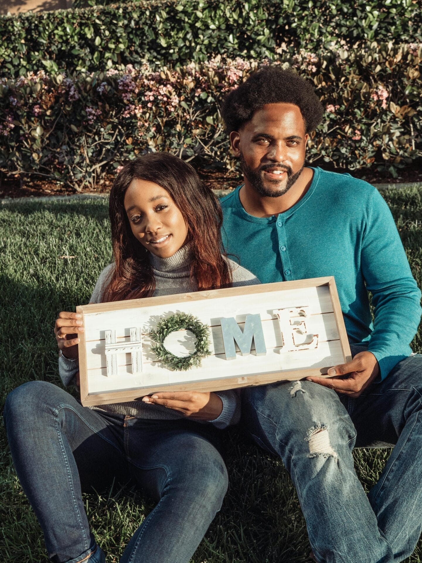 Happy couple sitting outdoors holding a home sign, symbolizing new beginnings and real estate celebration.